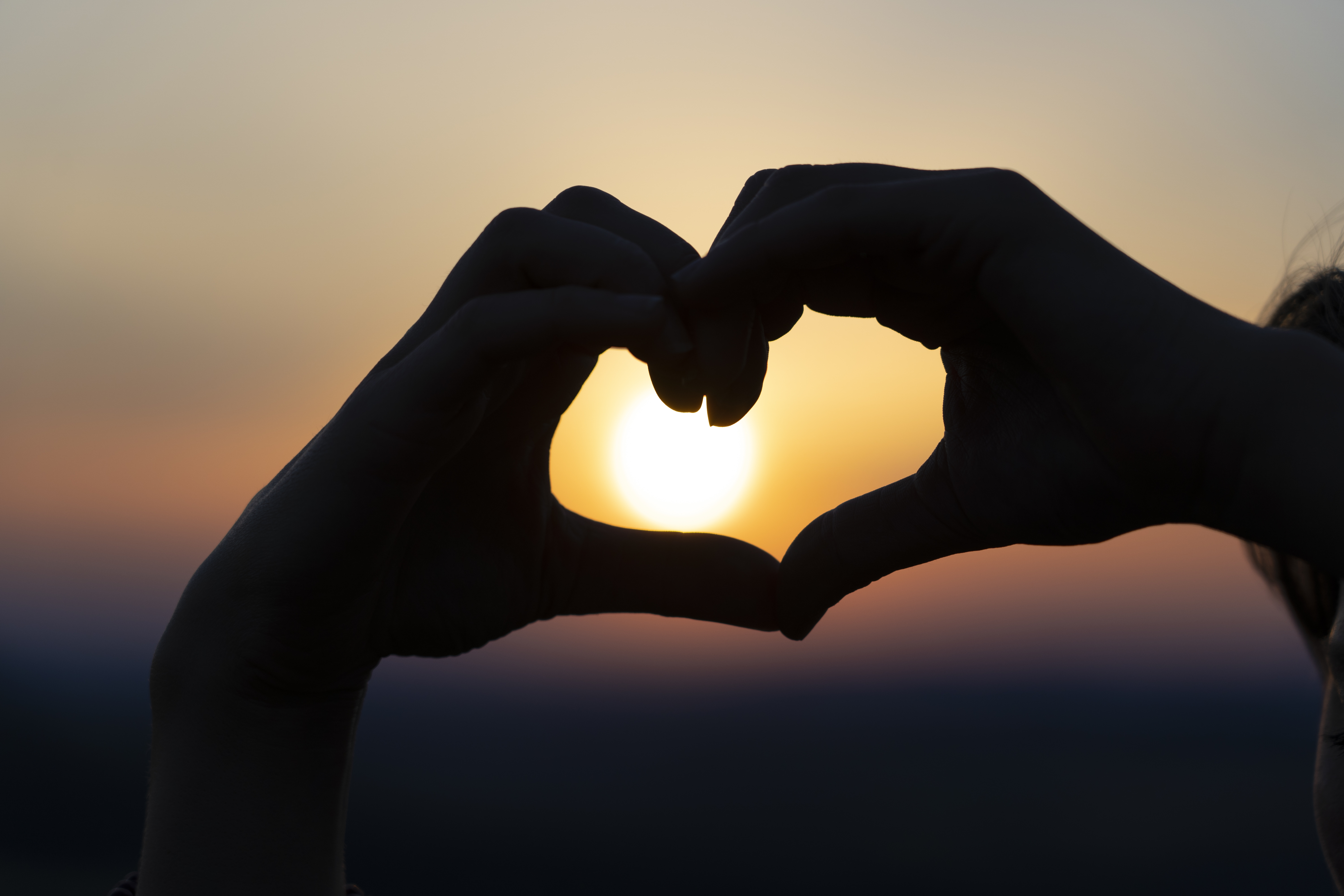 Silhouette of hands forming a heart on a sunset sky background